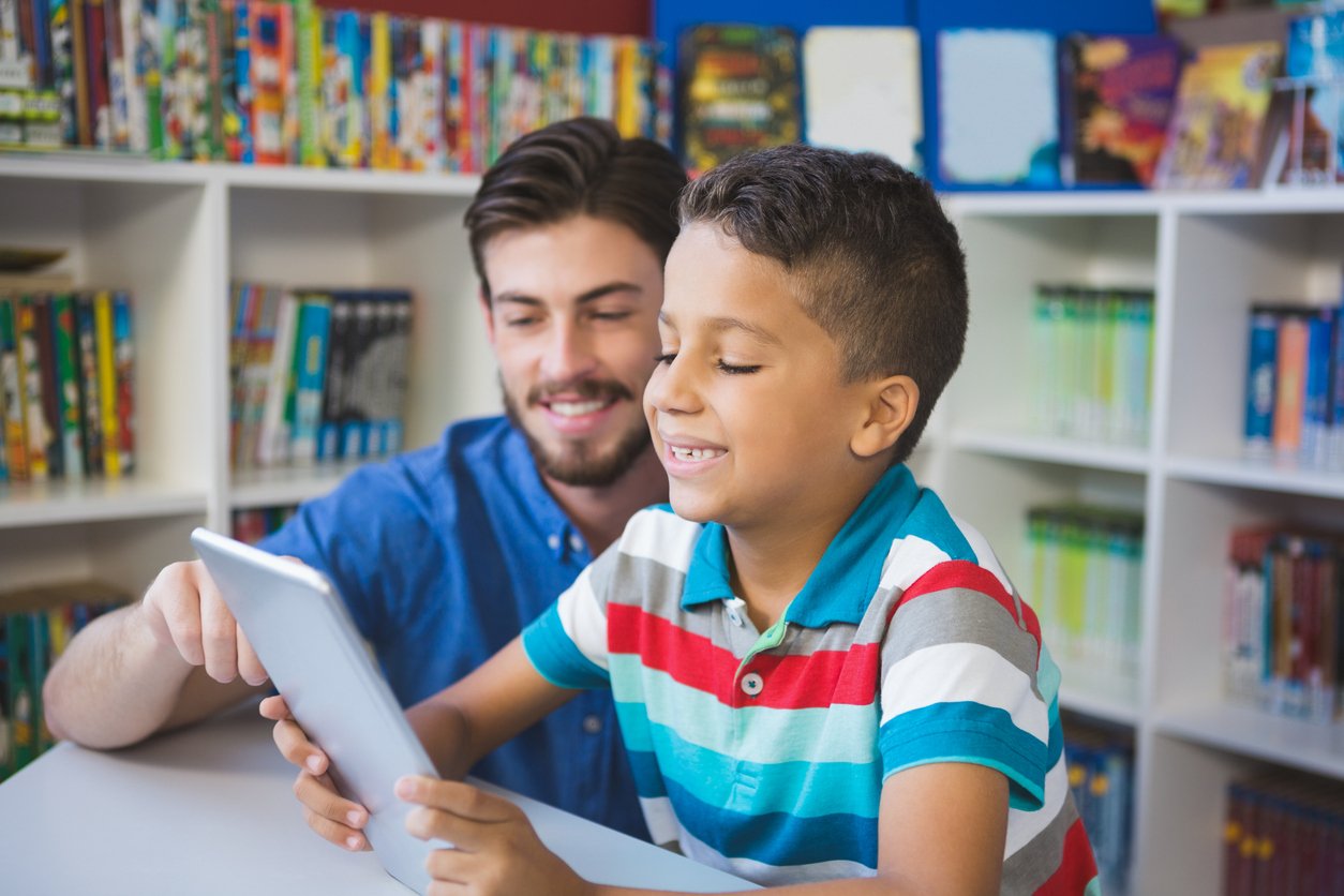 Educational assistant helping a child using digital tablet
