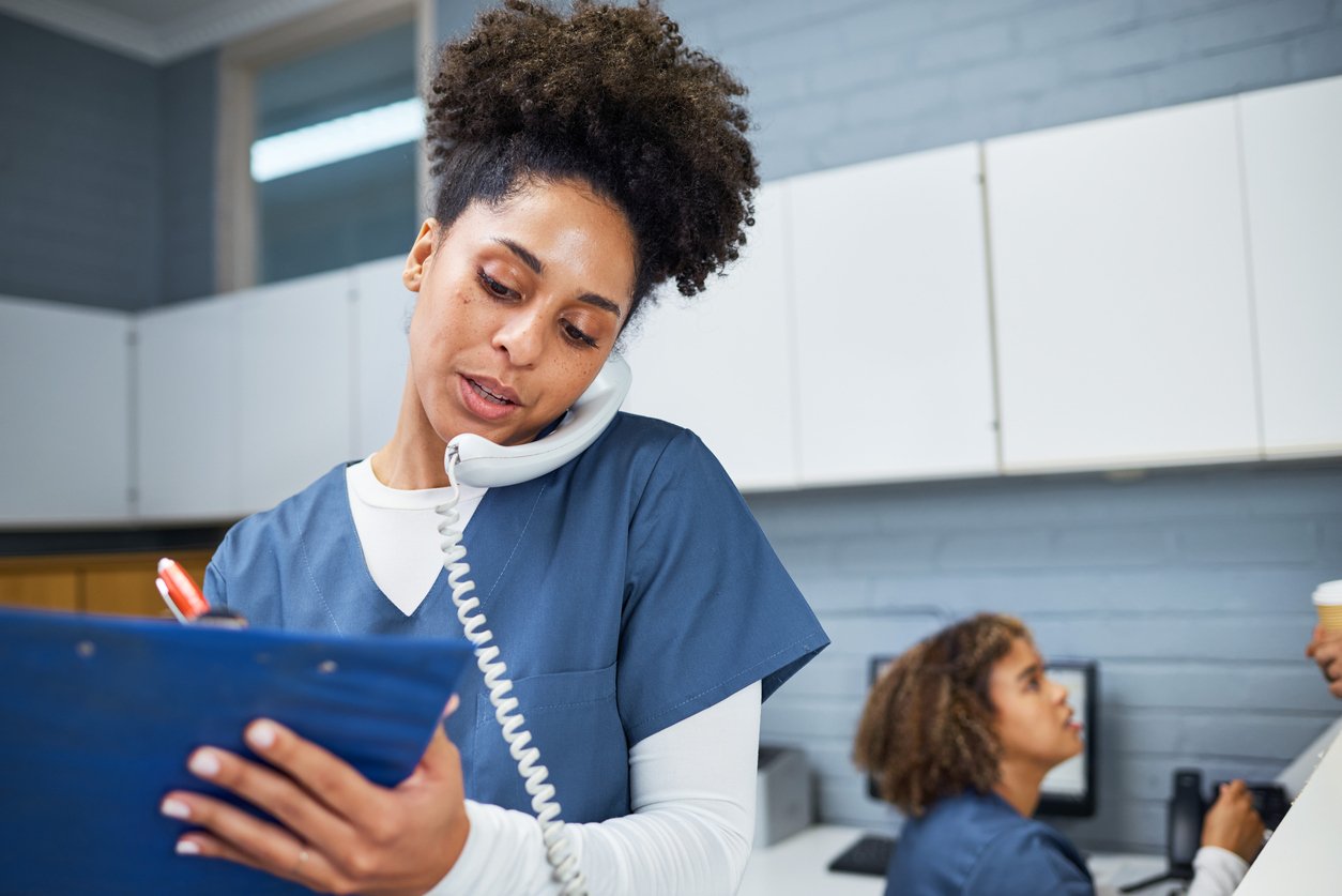 Medical office administrator taking notes while using phone