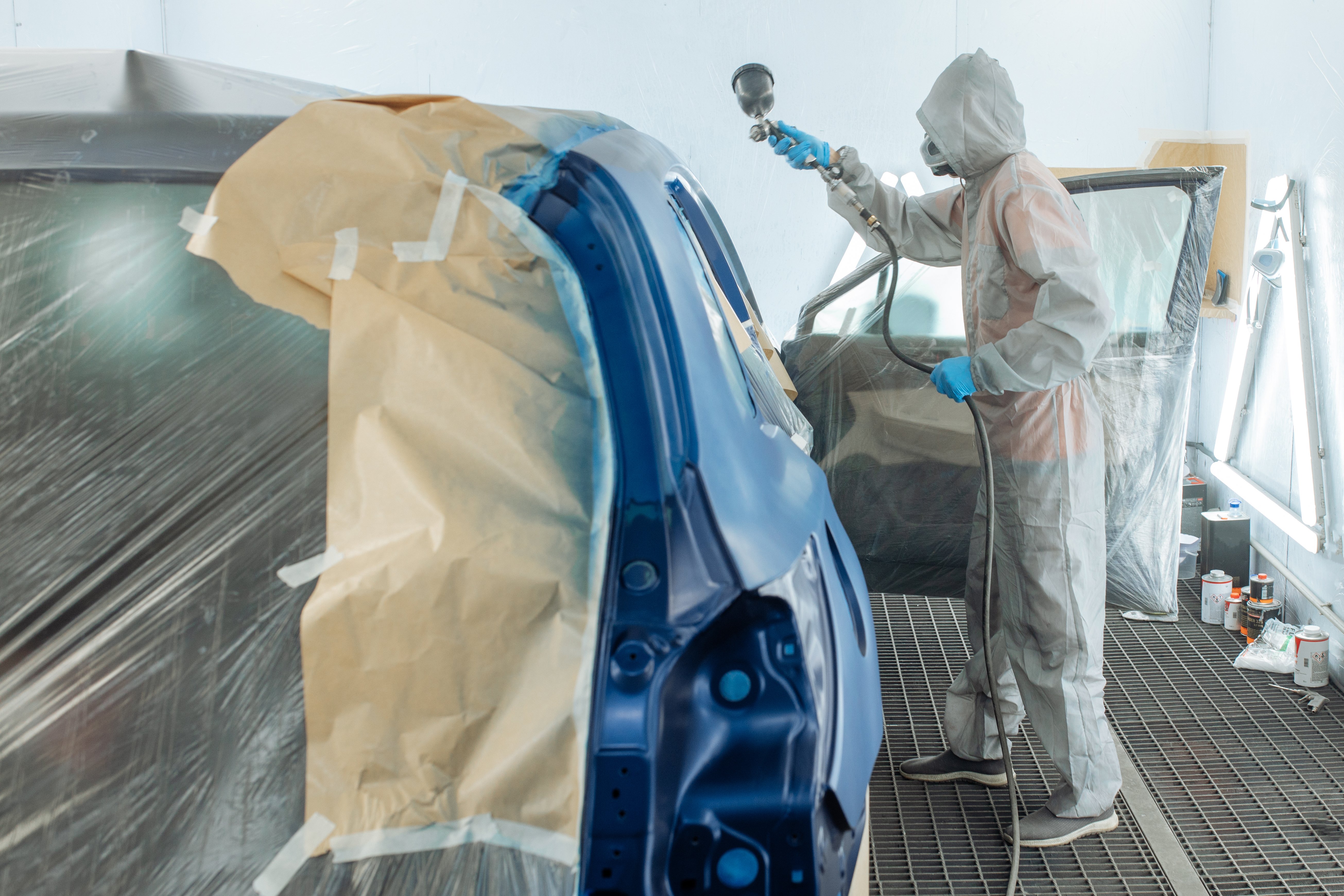 Worker in protective gear applying paint to vehicle