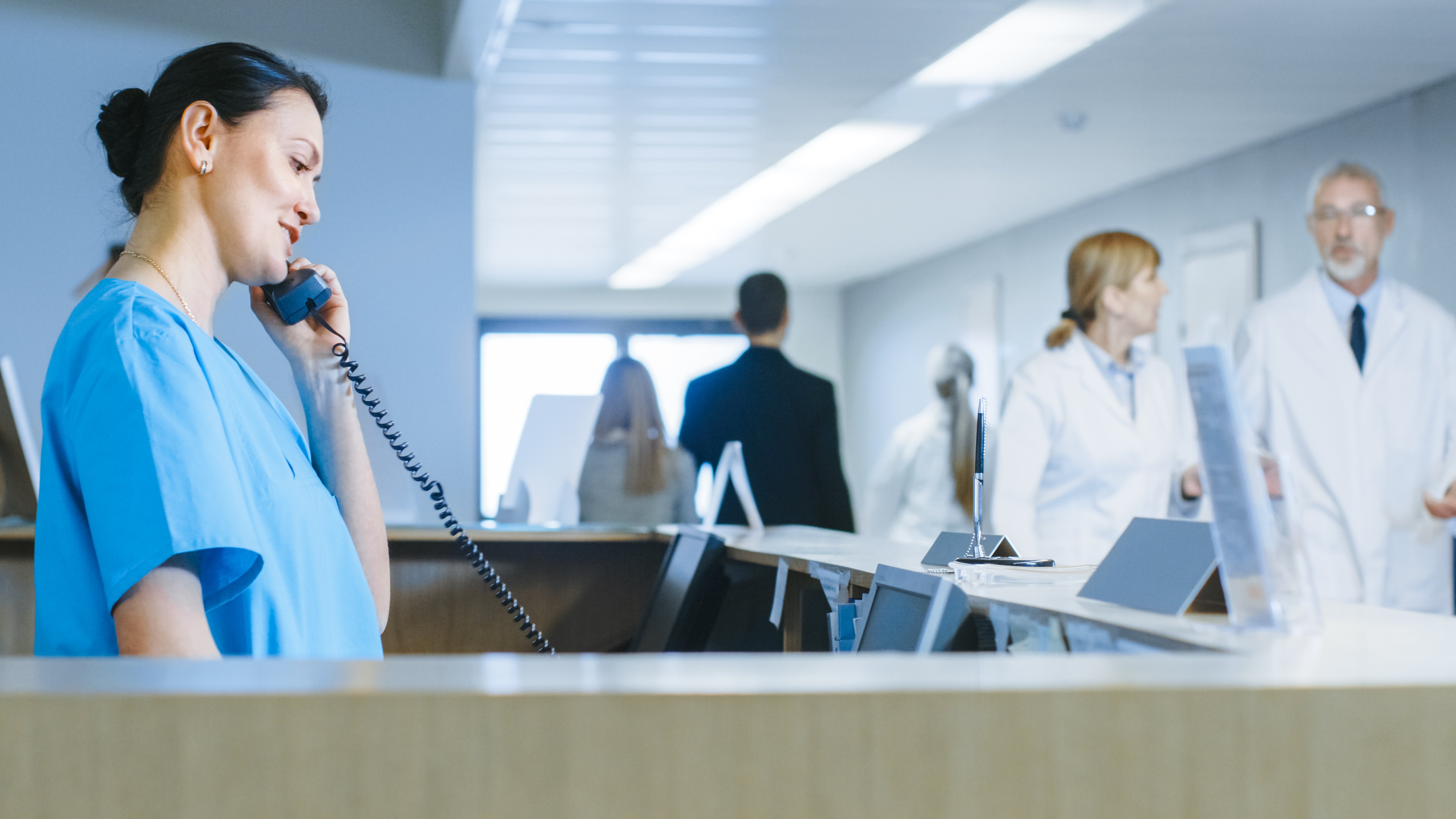 Medical office assistant standing and talking on phone in busy clinic