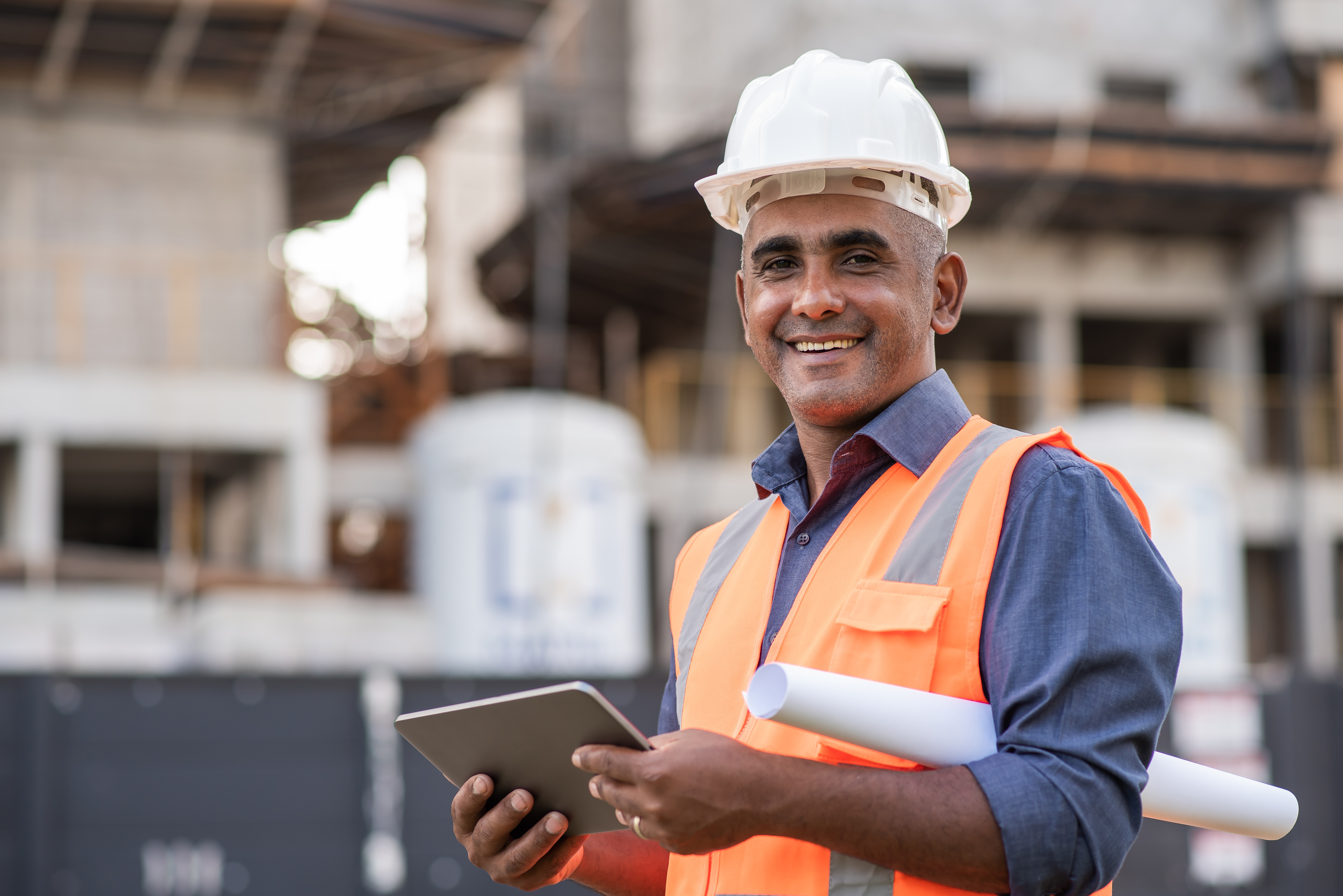 Smiling construction manager holding tablet and technical drawings