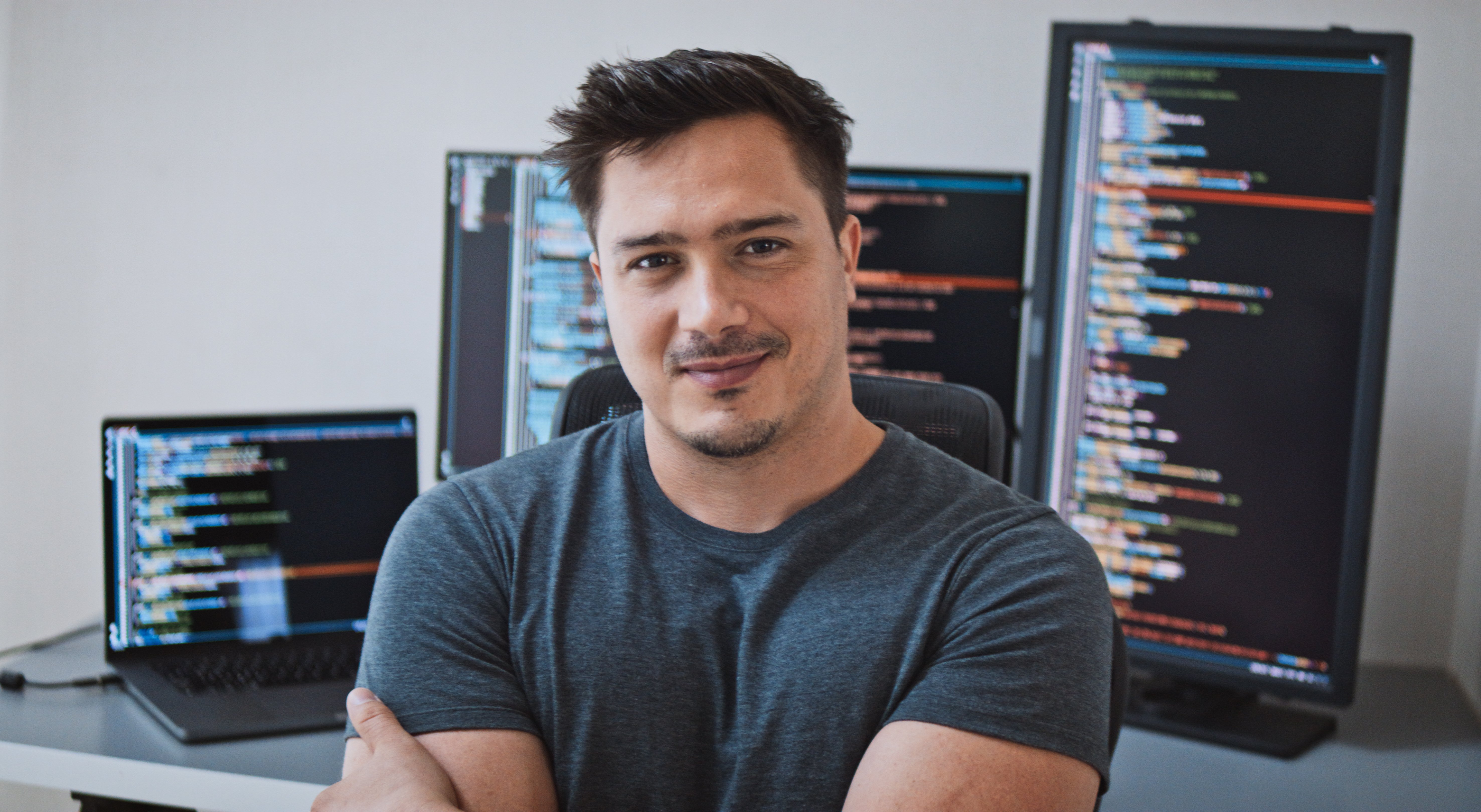 Data scientist sitting with arms crossed in front of multiple monitors