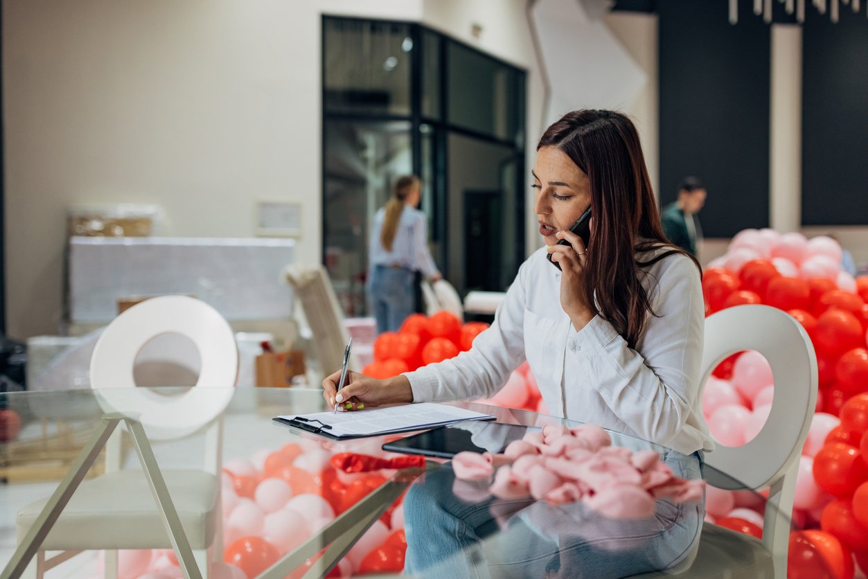Event manager sitting at table in banquet space, with balloons all around
