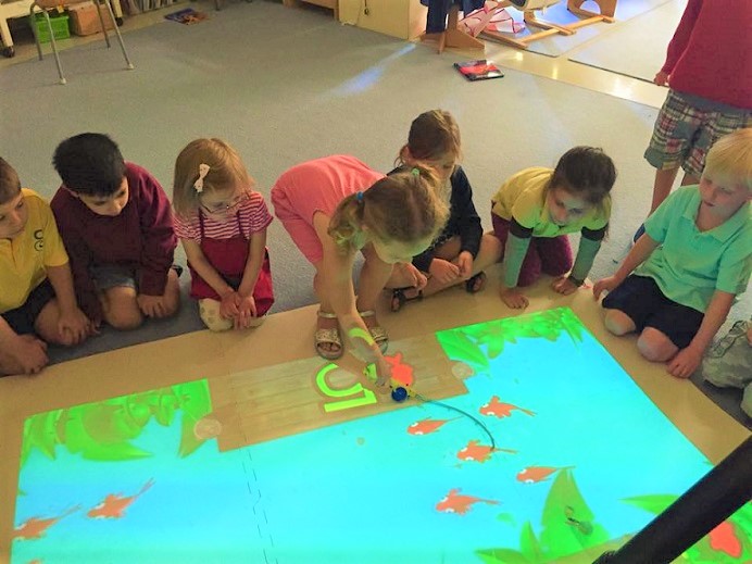 Group of young students sitting on classroom floor looking at fishing game