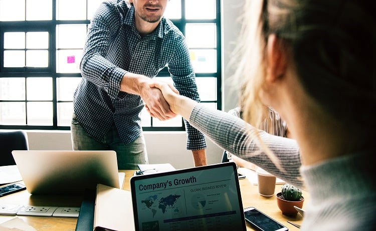 Man and woman shaking hands across a table at an interview