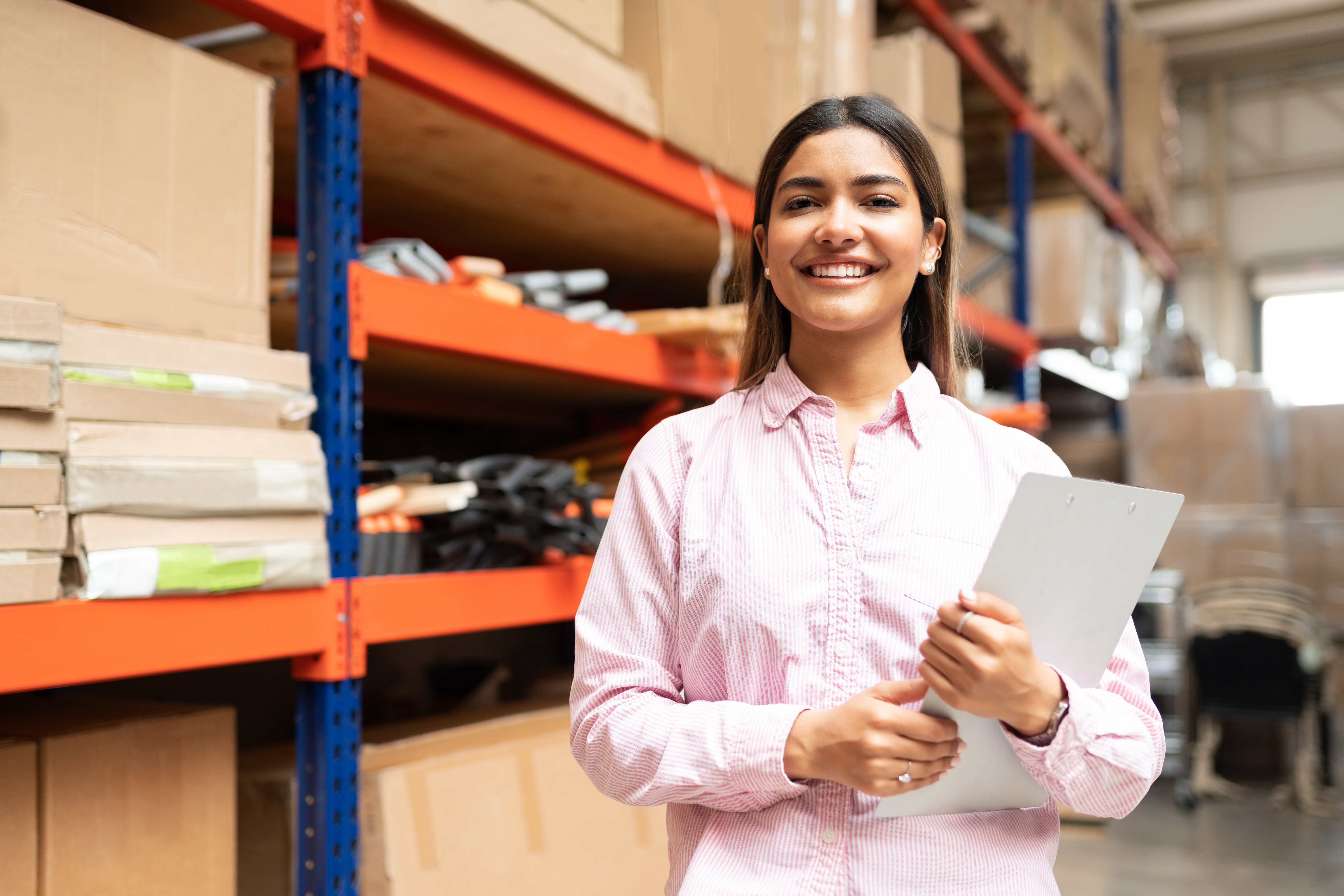 Smiling woman standing in warehouse holding inventory clipboard