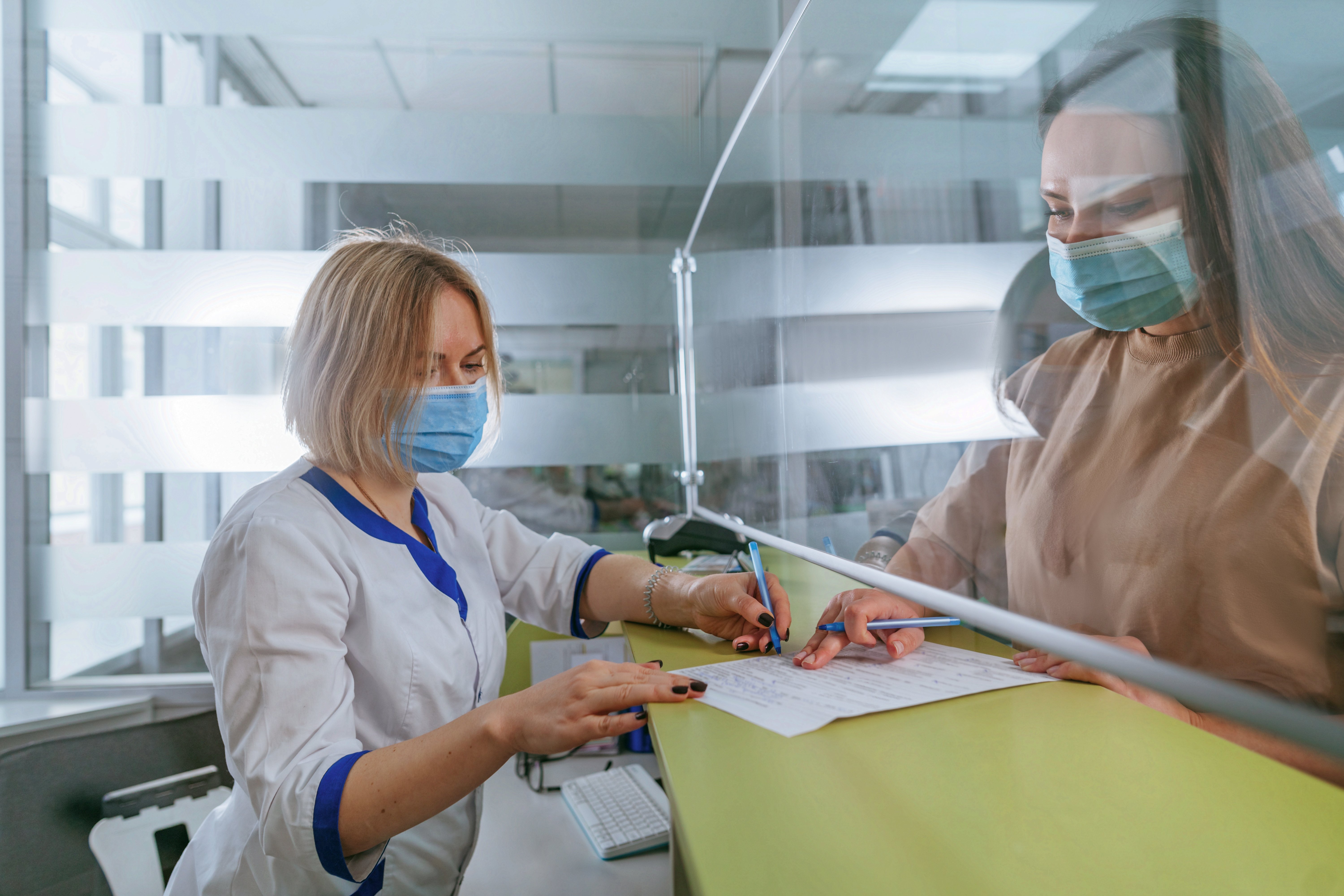 Masked assistant explaining to new patient how to fill in registration form