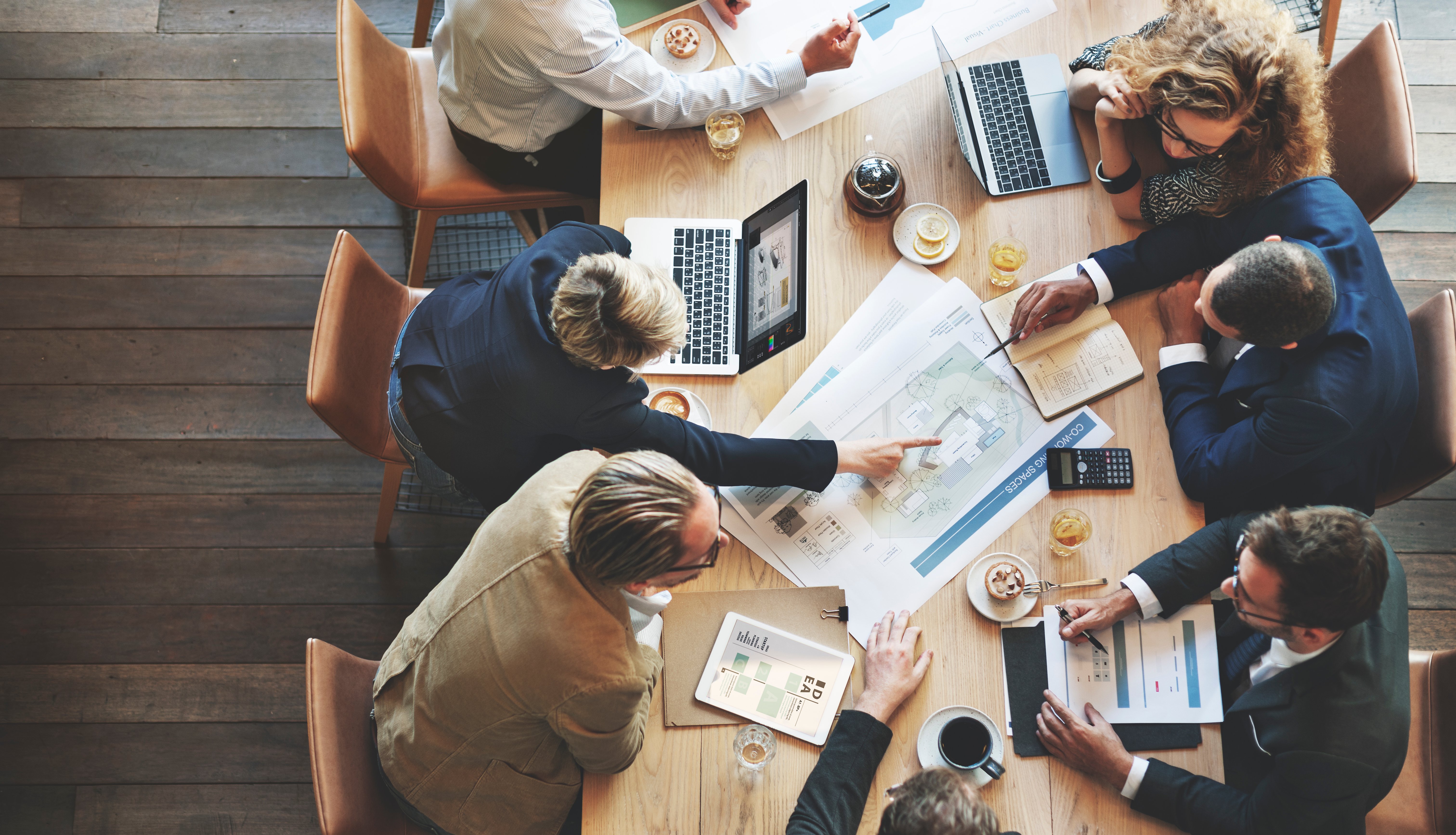 View from above of a group of people gathered around a table with papers, laptops, and snacks