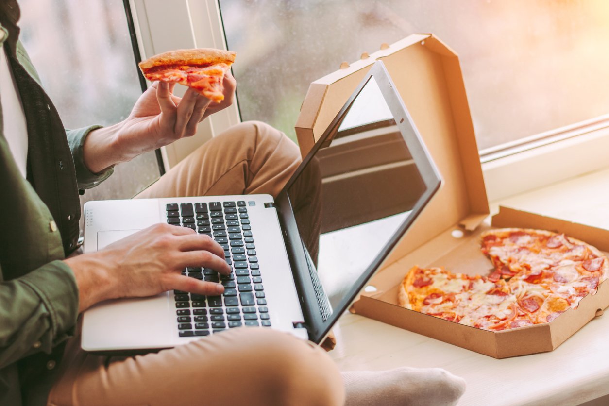 Man eating pizza while balancing computer on his lap