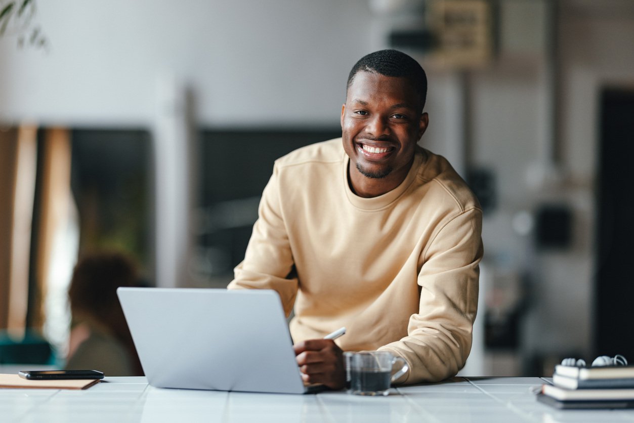 appy student looking at camera while sitting at laptop