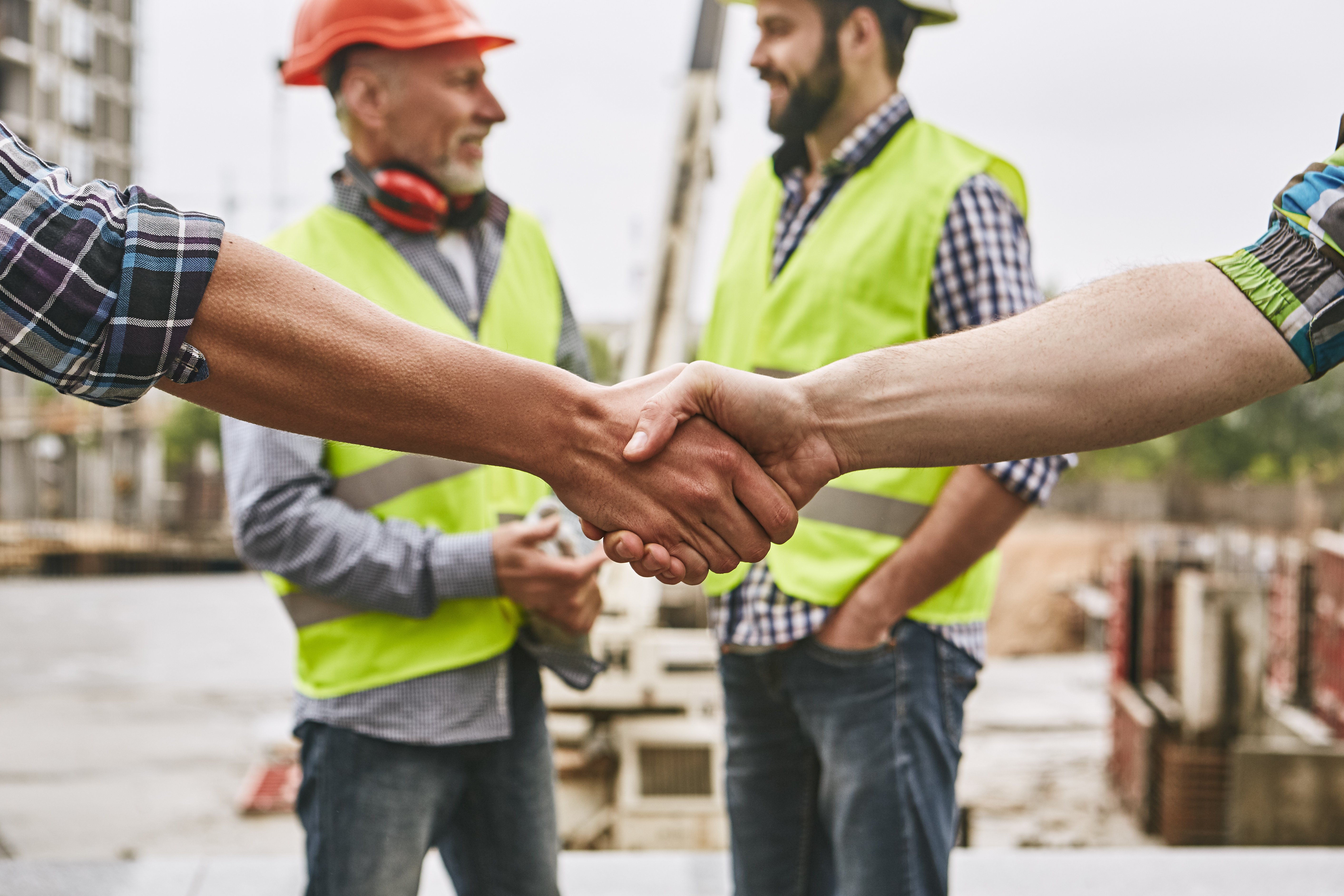 Close up of handshake, with construction workers in background