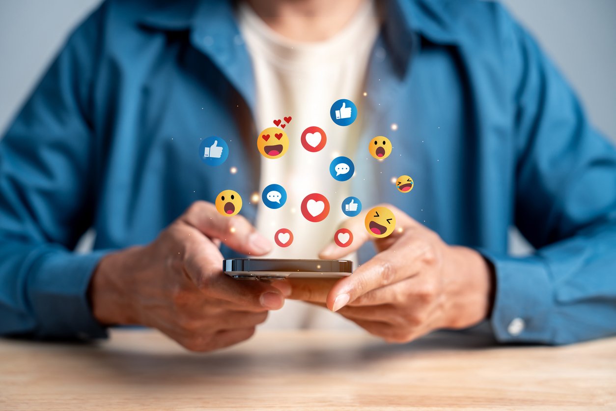 Man holding a smartphone with emoji icons in the foreground