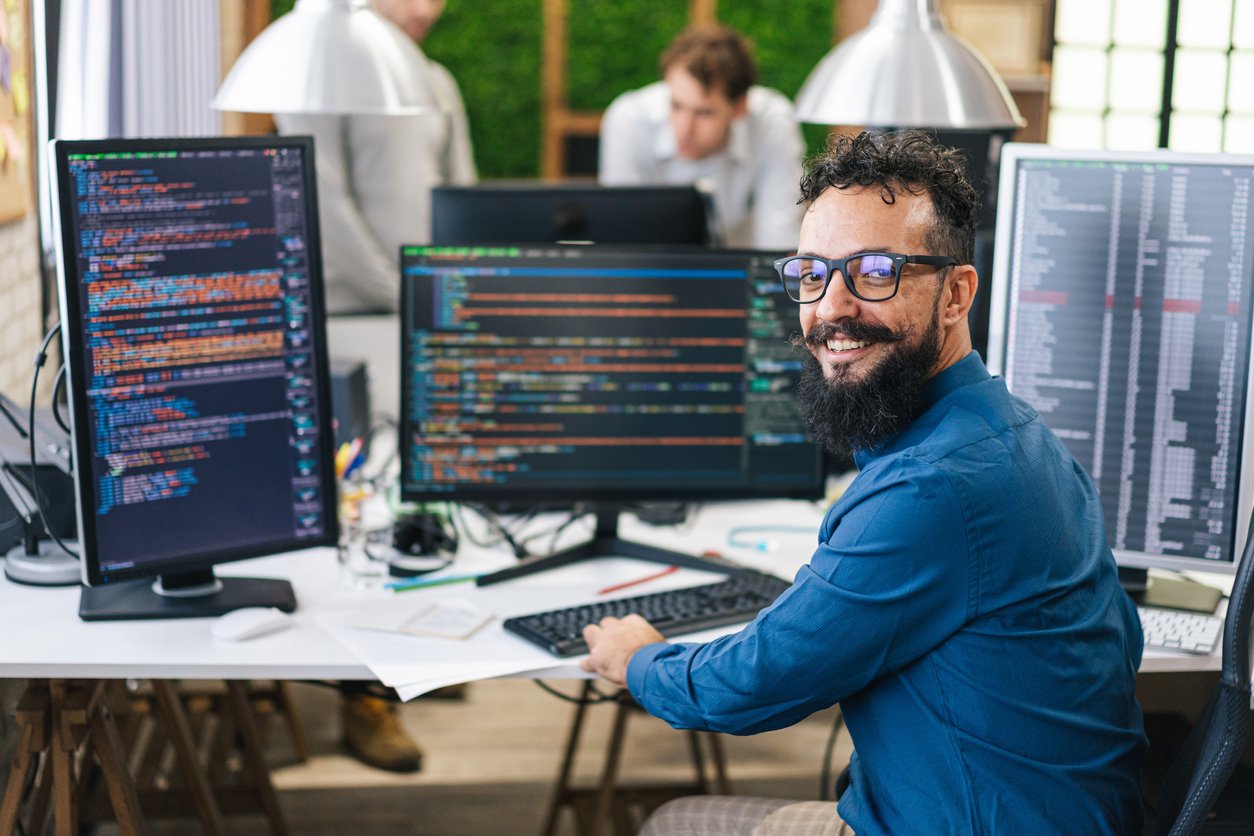 Smiling programmer sitting in front of multiple monitors