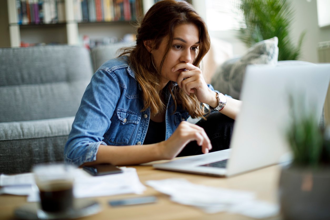 Woman sitting in front of laptop with hand on her mouth