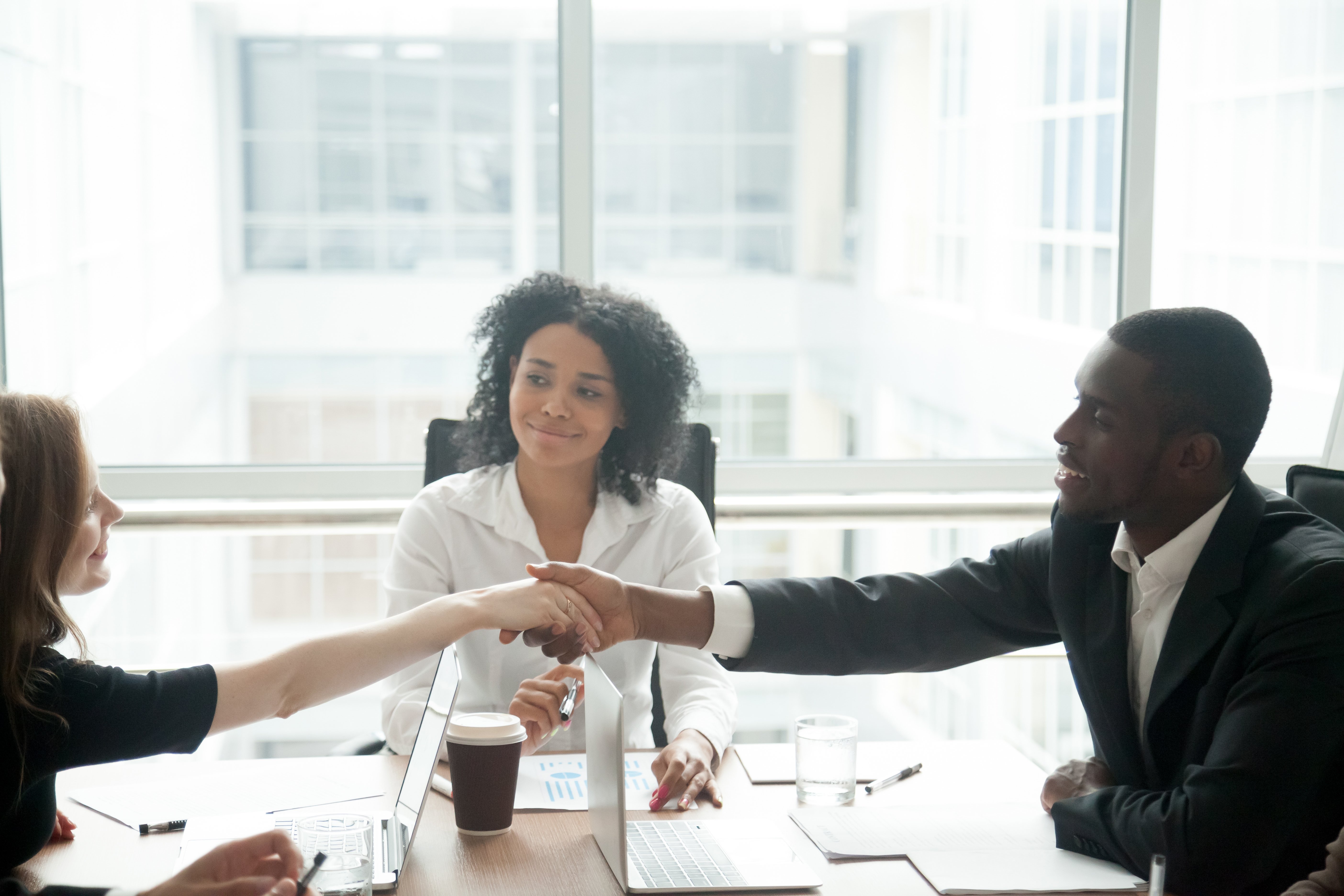 Two people reaching across a desk to shake hands in front of a smiling mediator