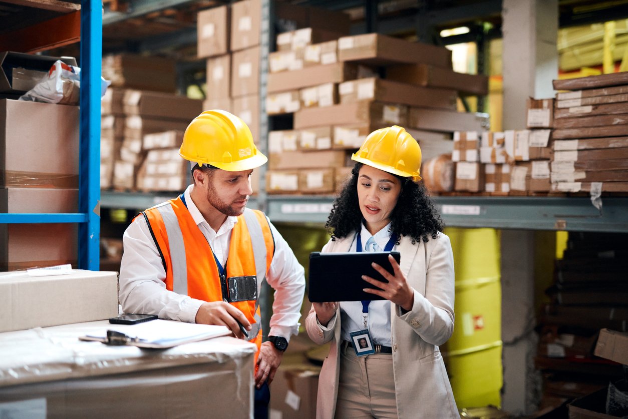 Two workers wearing hard hats talking in a warehouse