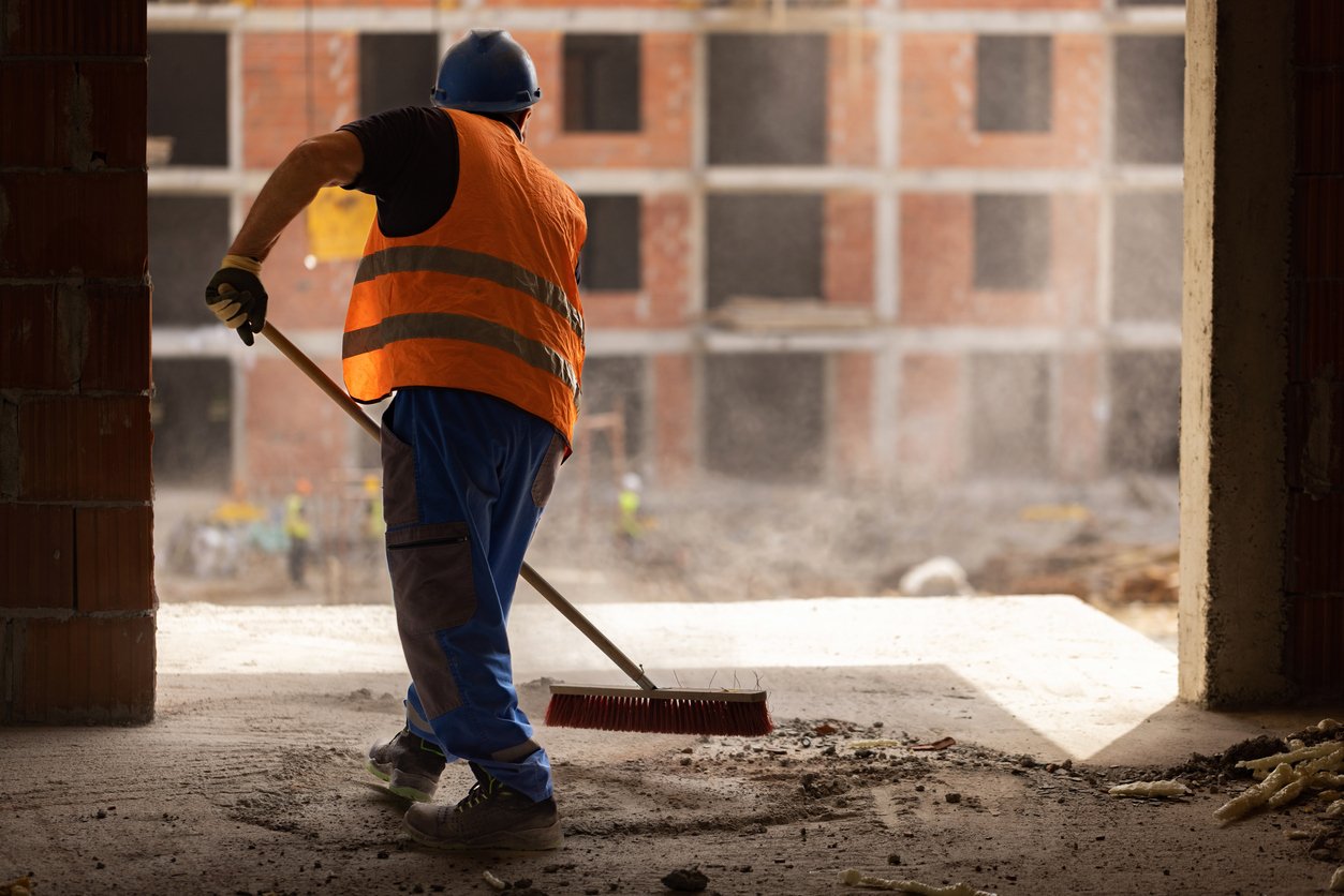 Construction worker using broom to clean the dust on a site