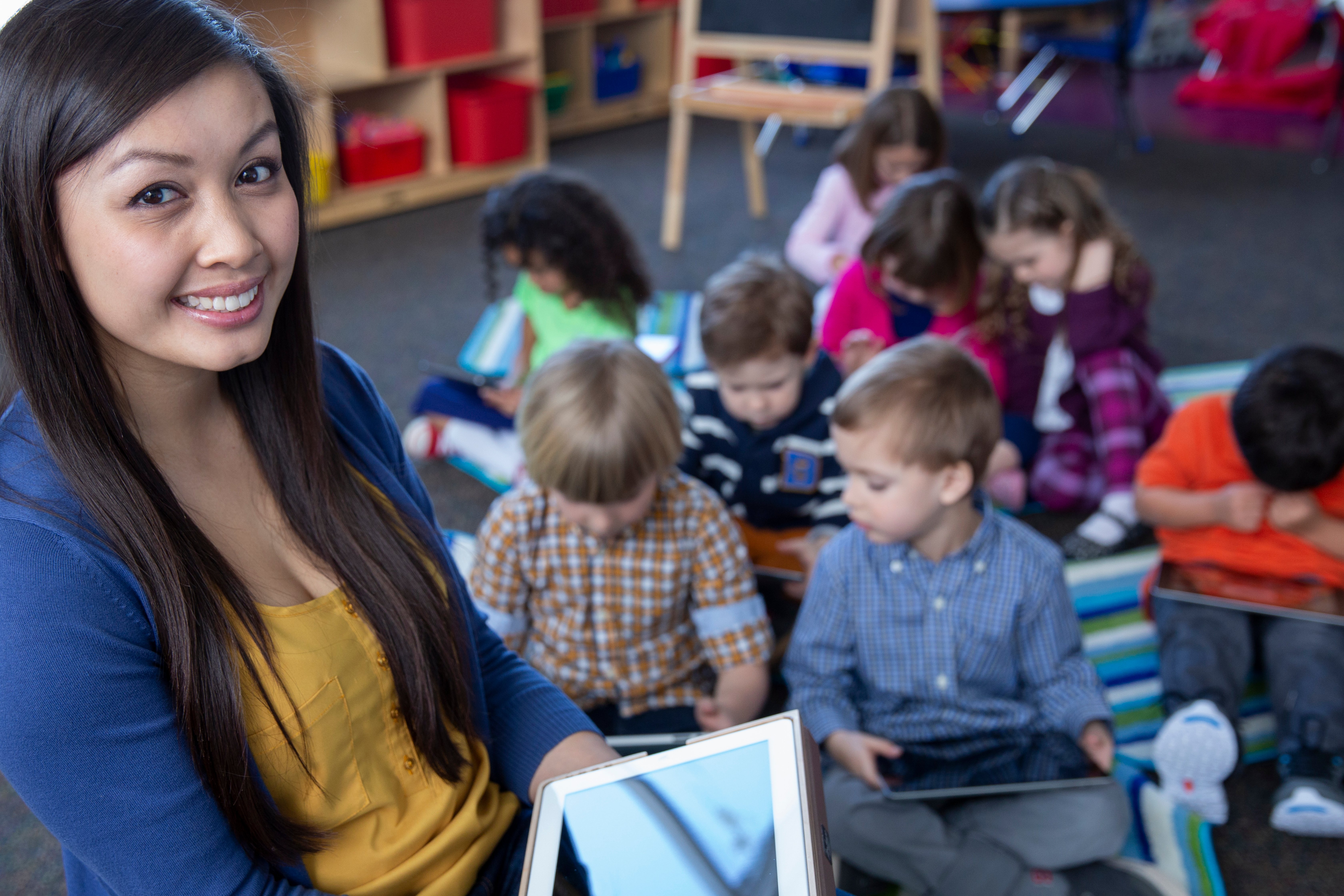 Smiling preschool teacher with student and tablets