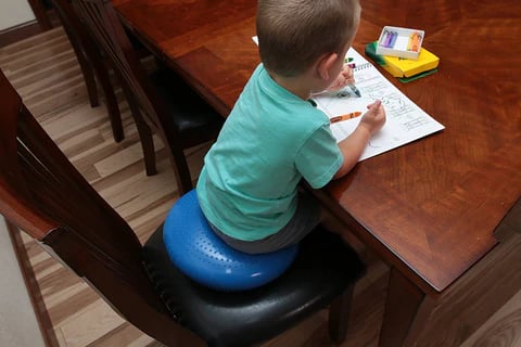 Young boy sitting on wiggle seat cushion while colouring