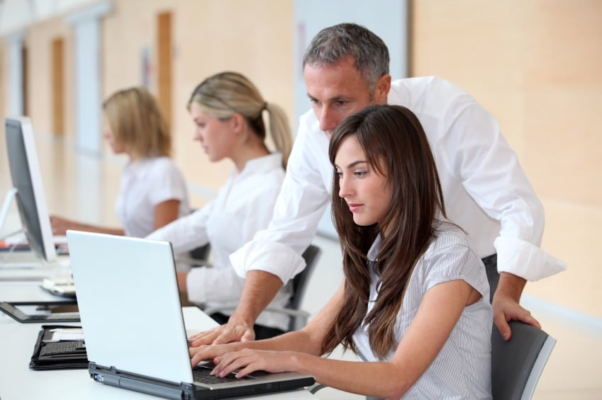 An intern working on a laptop getting help from a mentor