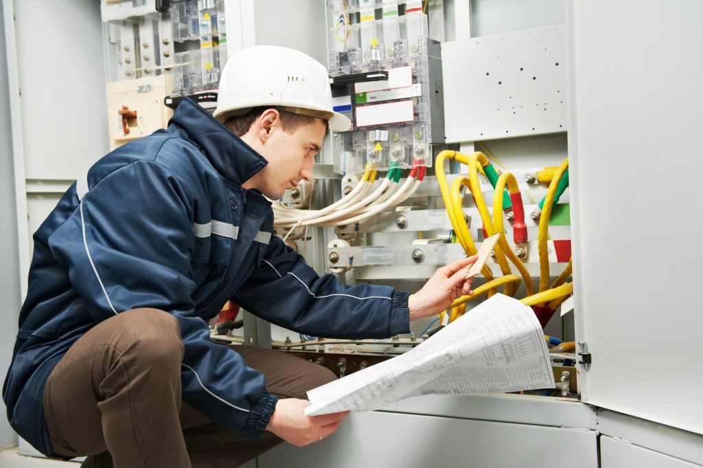Electrician inspecting the cabling connection of a high-voltage power electric line in an industrial distribution fuseboard