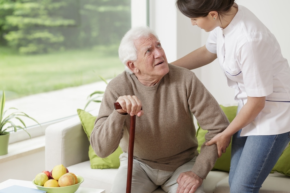 White-haired man holding cane and looking up at health care aide