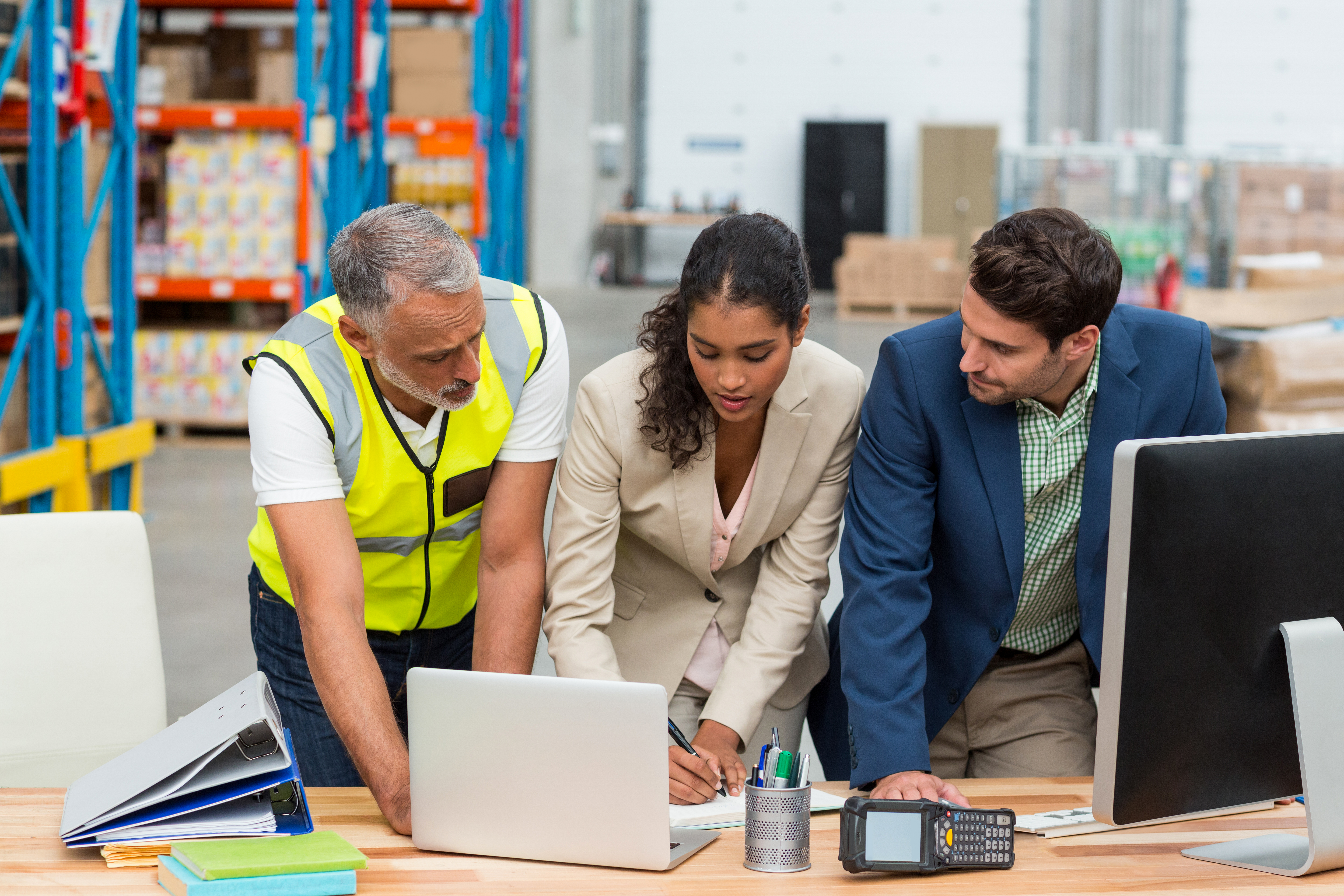 Three workers gathered around a laptop in a warehouse