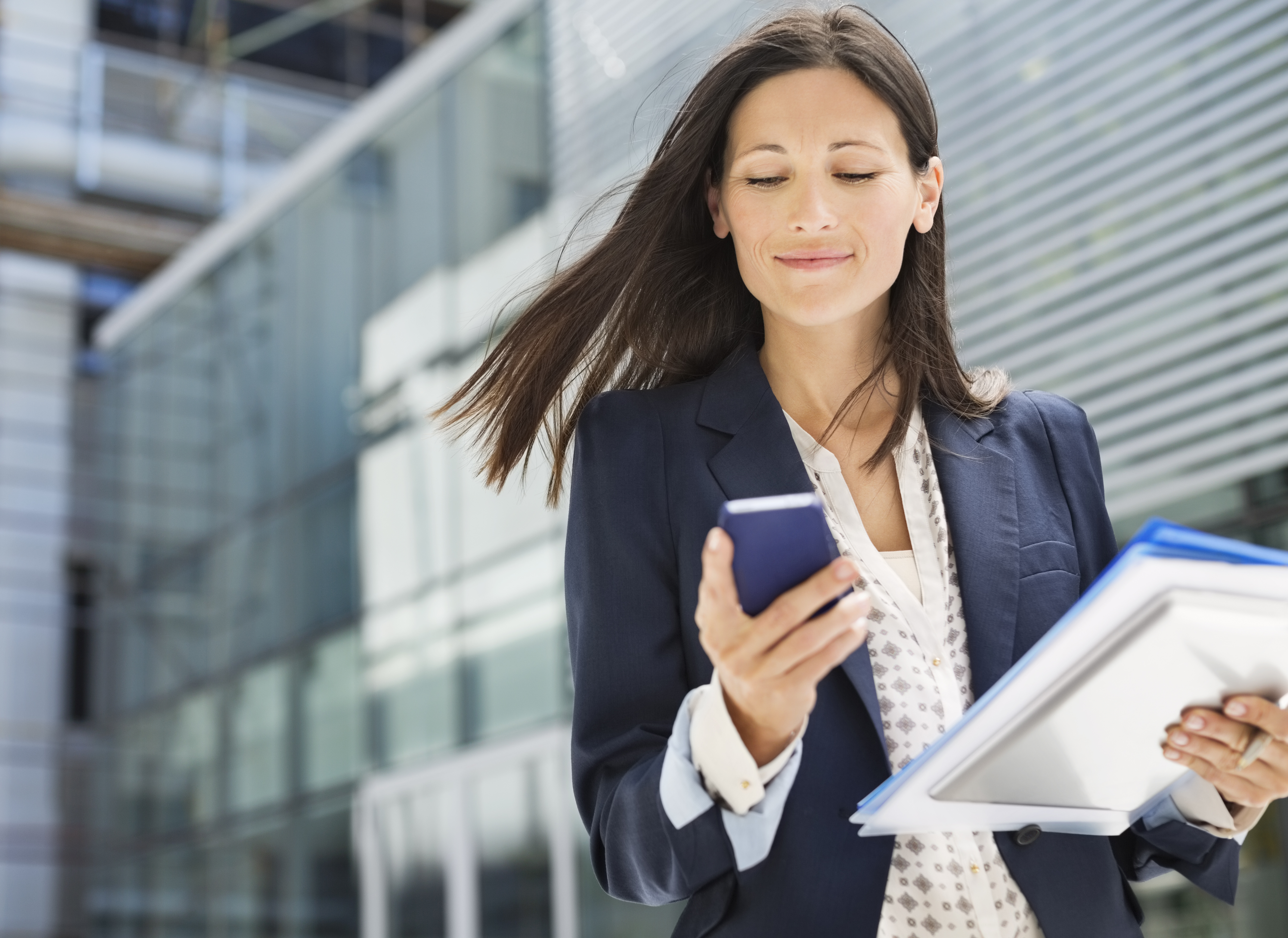 Businesswoman carrying documents and looking at phone