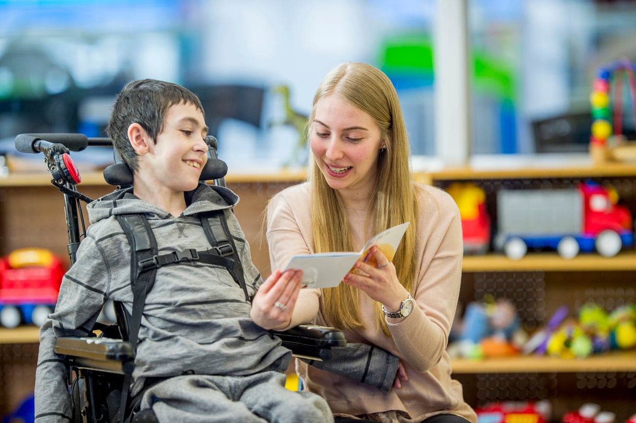 Educational assistant reading a story to a boy in a wheelchair