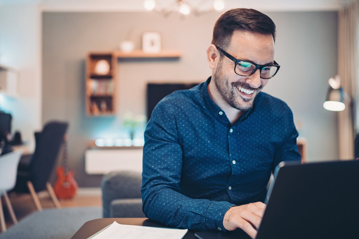 Homme souriant travaillant de son domicile sur ordinateur portable