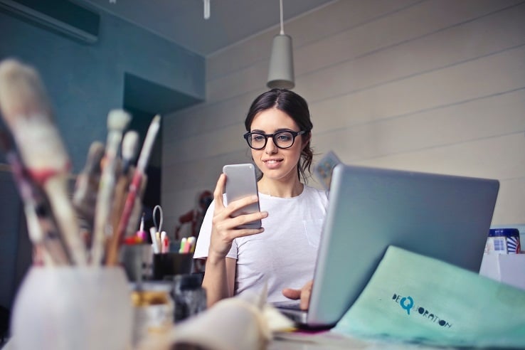 Woman sitting in front of computer looking at smartphone