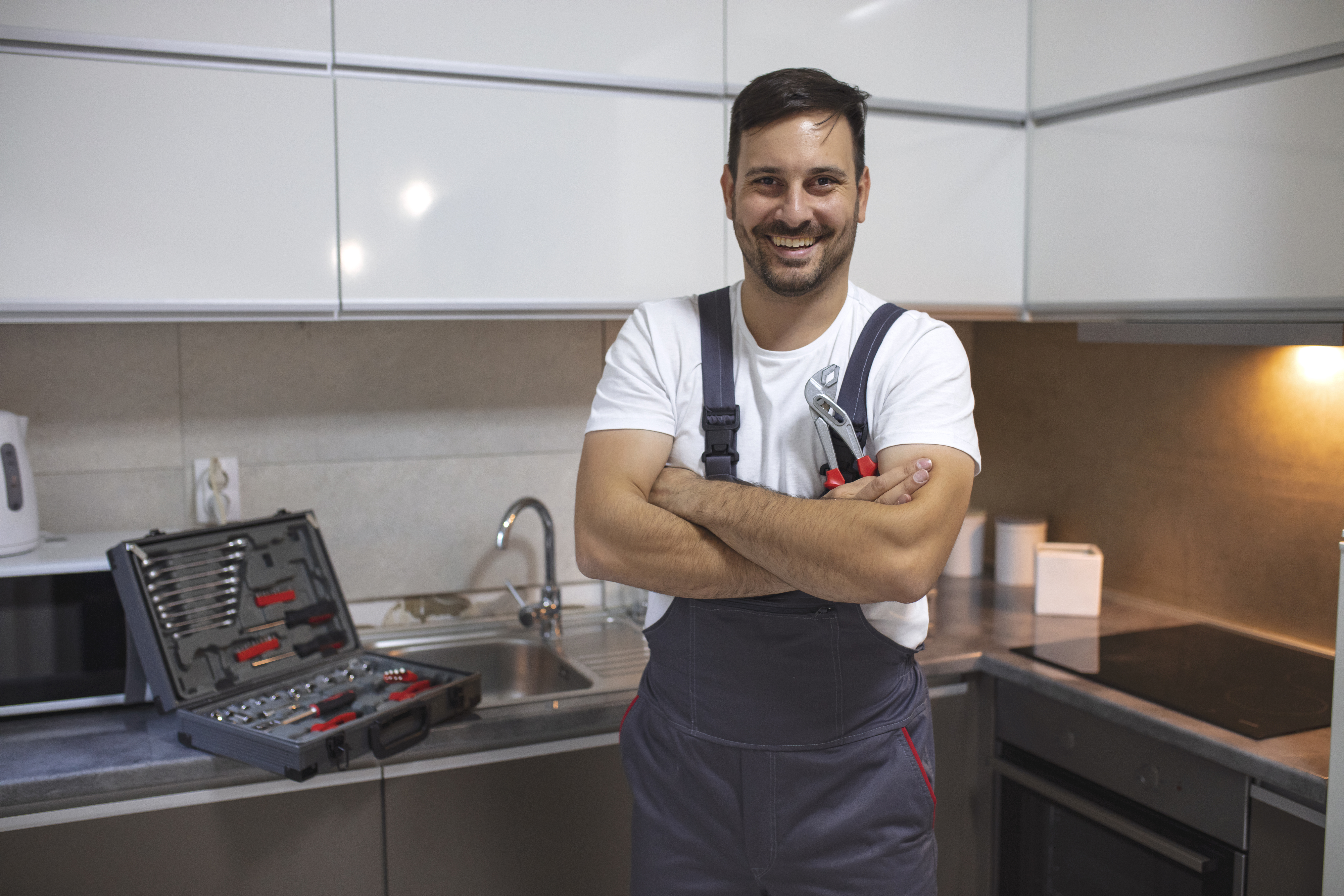 Smiling plumber standing with arms crossed in kitchen