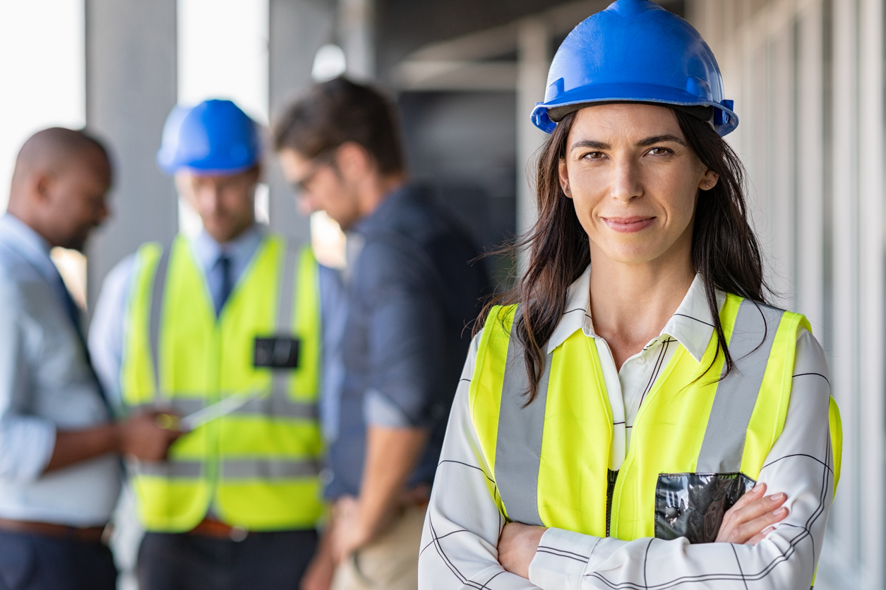 Woman in hard hat and safety vest standing with arms crossed 