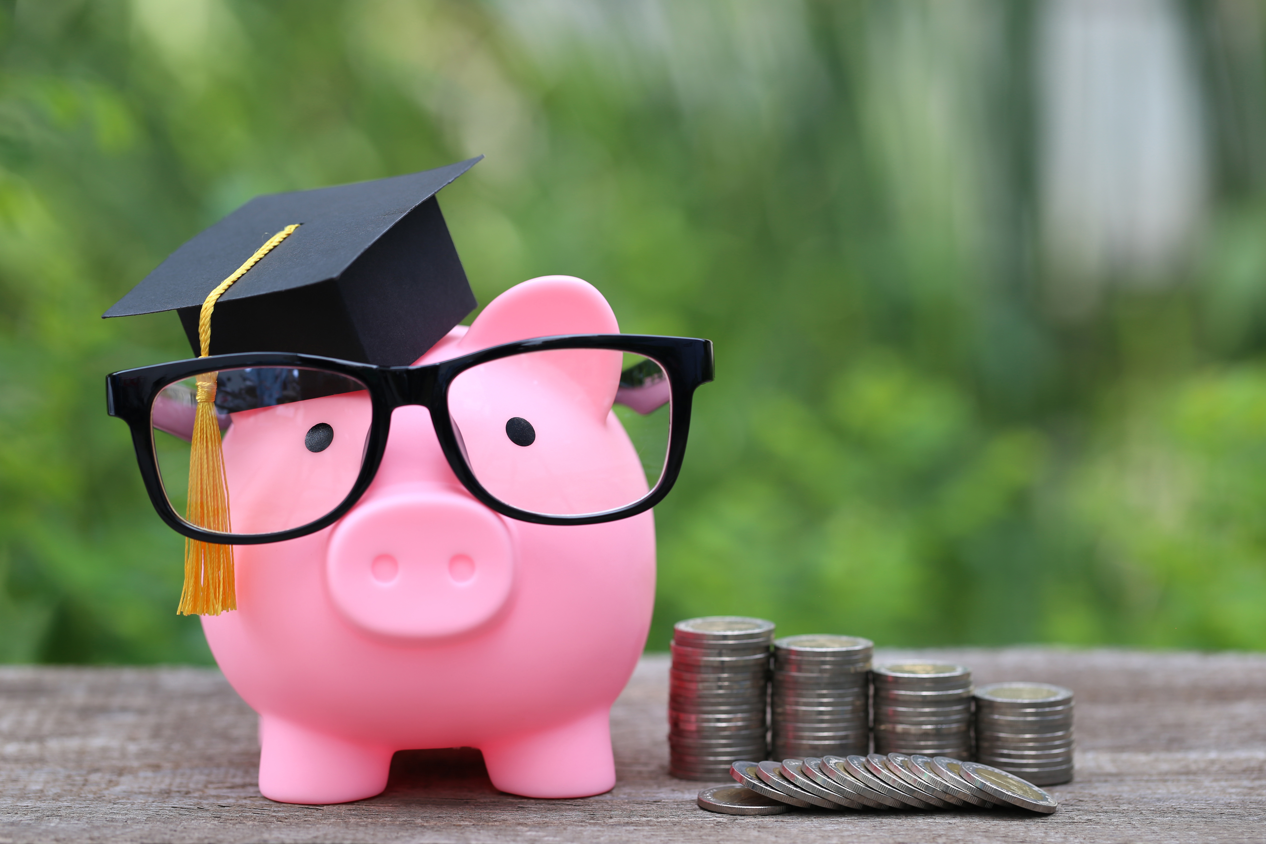 Piggy bank wearing glasses and a graduation cap next to stacks of coins