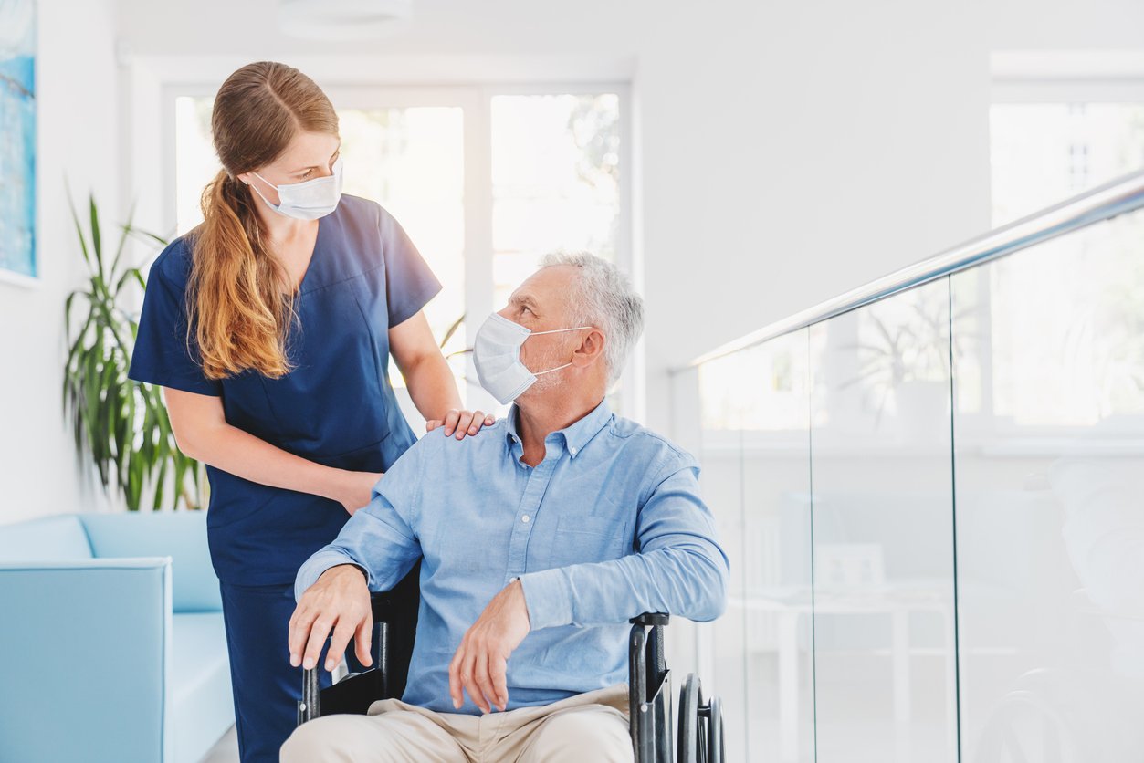 Young woman wearing scrubs looking down at a man in a wheelchair