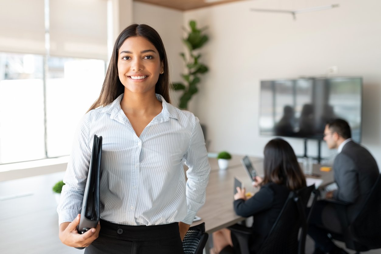 Smiling woman standing in office holding binder