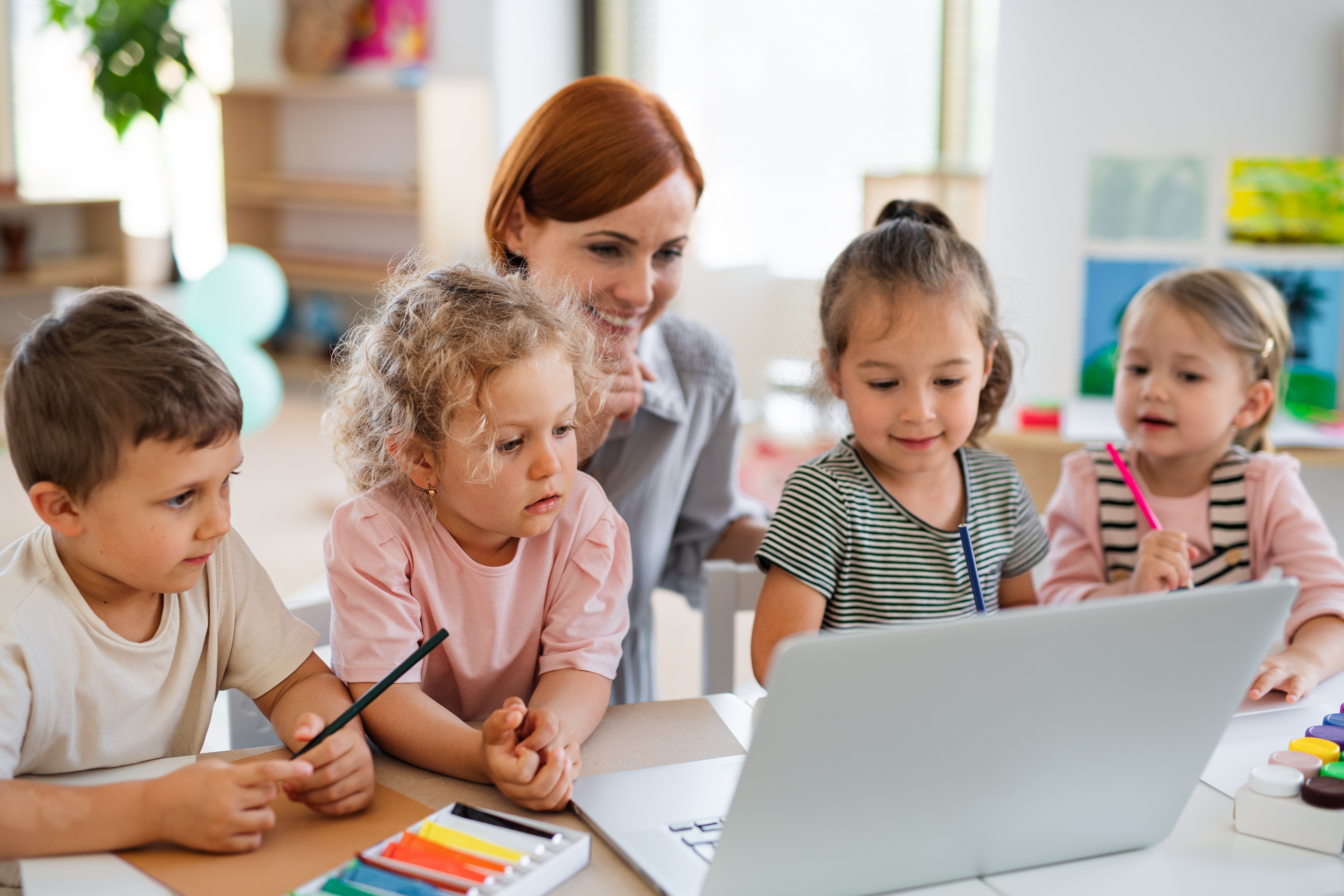 A group of preschool children with teacher in classroom using laptop
