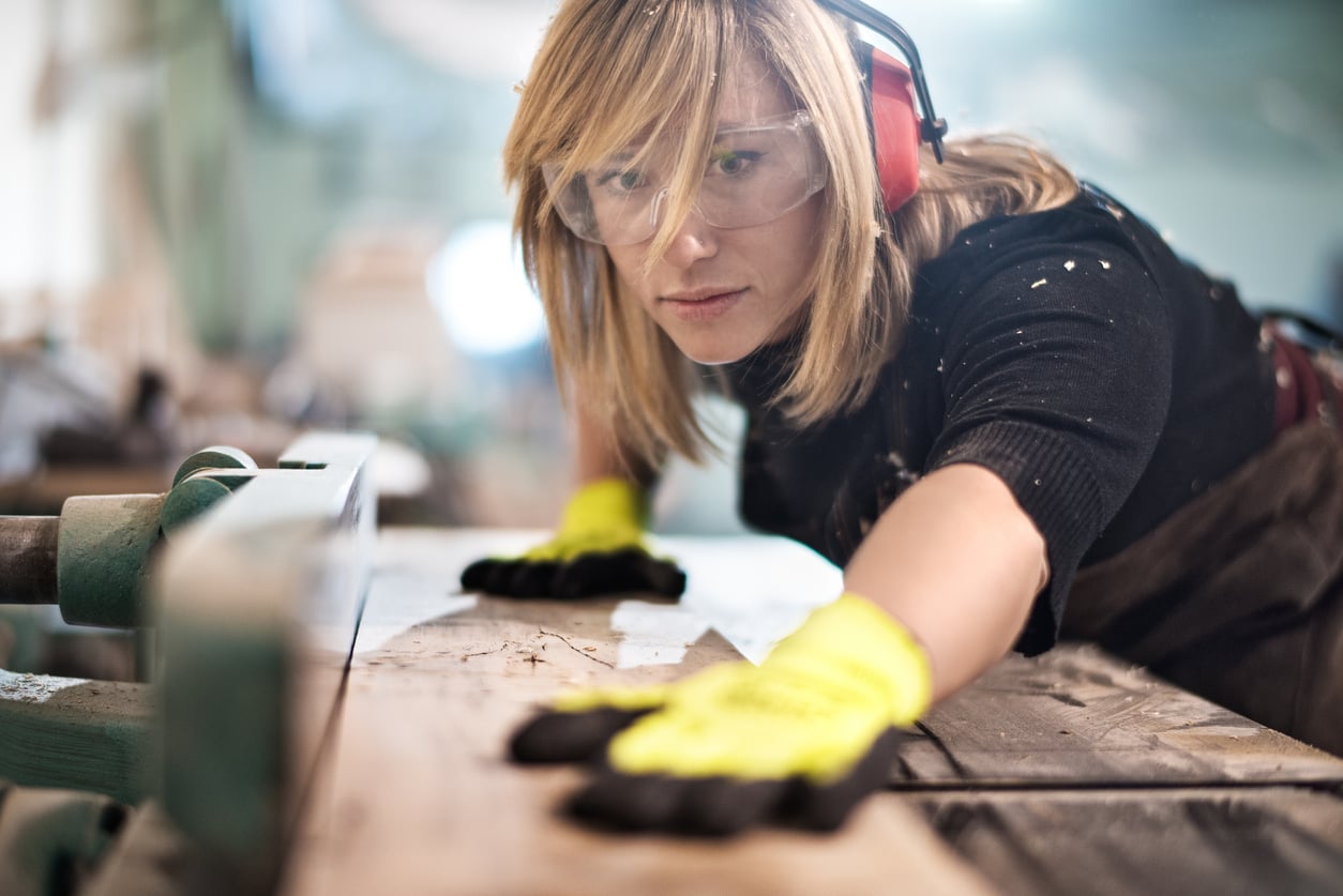 Carpenter wearing eye and ear protection while cutting a plank