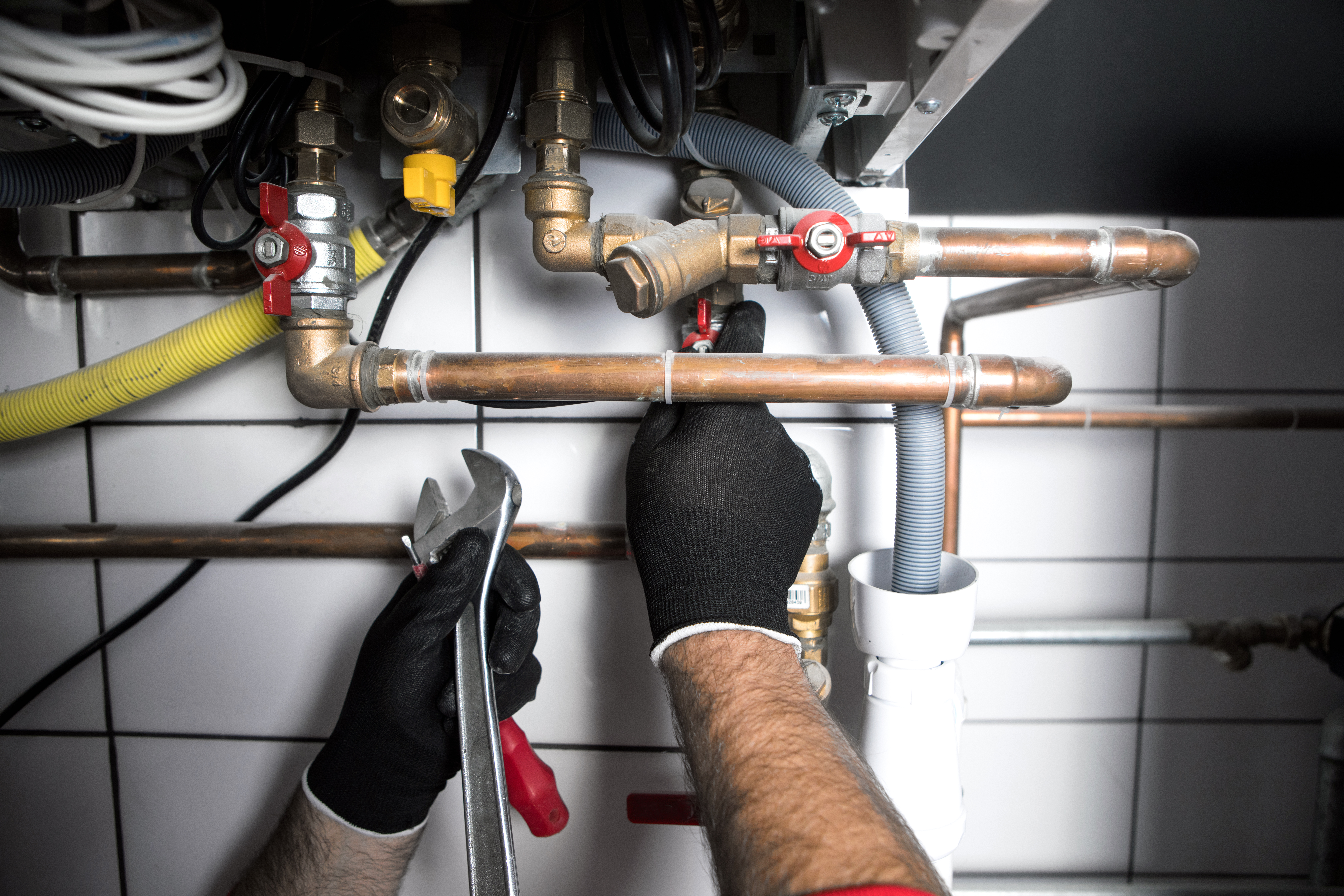 Hands of plumber holding wrench and working on pipes