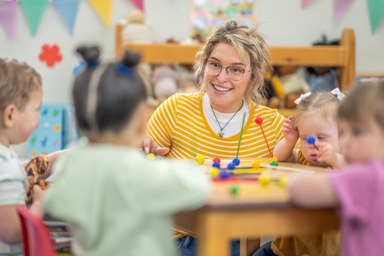 Small group of preschool children sit with their teacher at a table