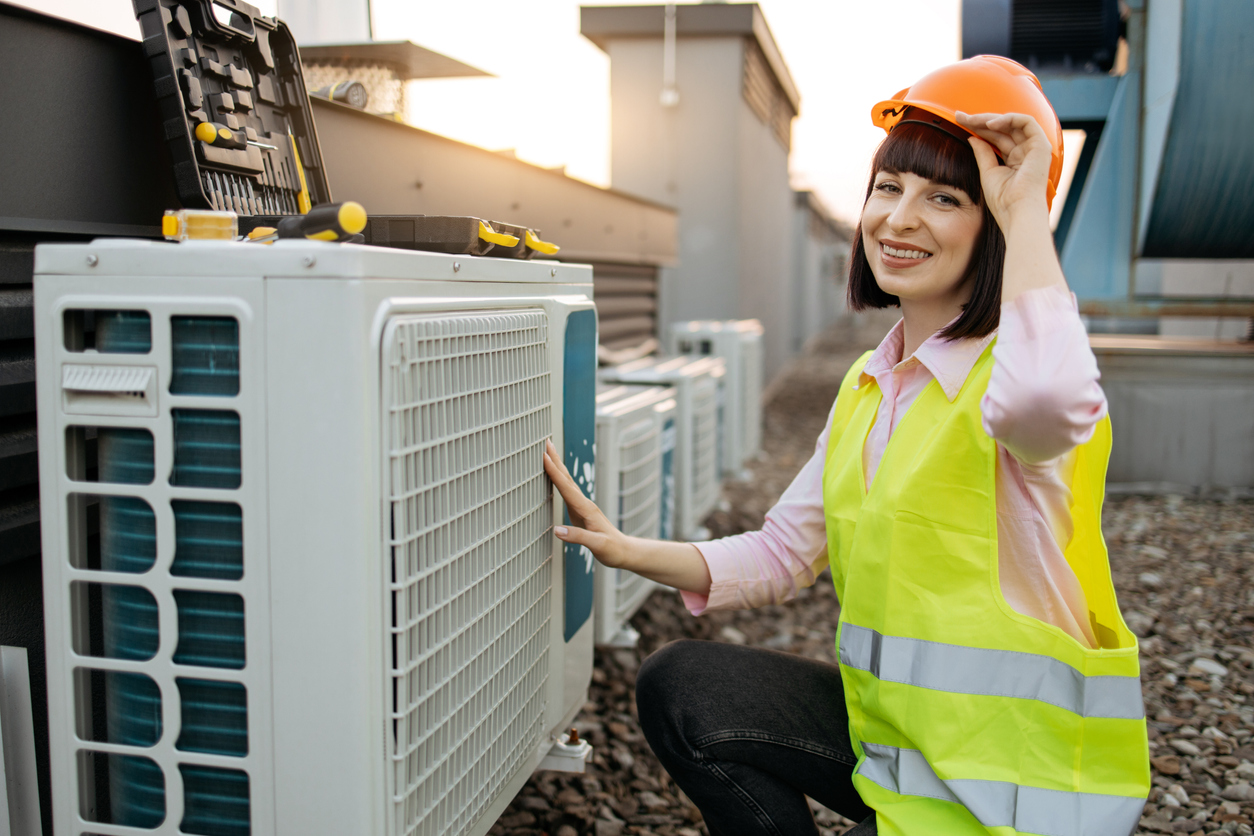 Woman adjusting hard hat while kneeling near air conditioner